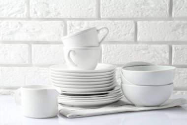 Different clean dishware on white table near brick wall