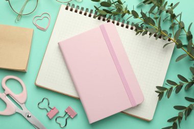 Turkuaz arka planda cilt klipleri, diğer kırtasiye malzemeleri, gözlükler ve yeşil dallar, düz konum