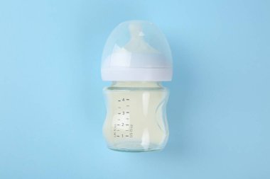 Açık mavi arka planda sütle beslenme şişesi, üst görünüm