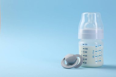 Açık mavi zemin üzerinde süt ve emzik ile beslenme şişesi, metin için boşluk