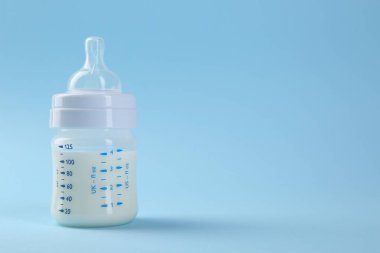 Açık mavi arka planda sütle beslenme şişesi, metin için boşluk