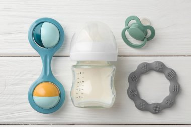 Süt, emzik, ip ve bebek çıngırağı ile beslenme şişesi beyaz ahşap masa, düz yatıyordu