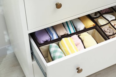 Organizers with folded clothes in drawer indoors, closeup