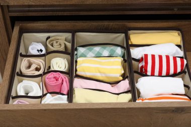 Organizers with folded clothes in drawer indoors, closeup