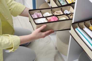 Kadın, farklı çoraplarla organizatörü evdeki rafa koyuyor, yakın plan.