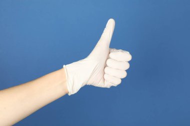 Tıbbi eldivenli doktor mavi arka planda baş parmak gösteriyor, yakın plan.