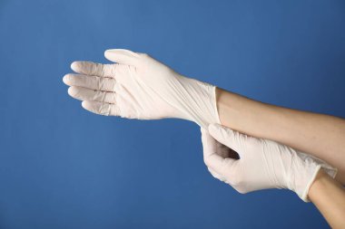 Doktor mavi arka plana tıbbi eldiven takıyor, yakın plan.