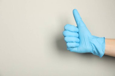 Tıbbi eldivenli doktor açık gri arka planda baş parmak gösteriyor, yakın plan. Metin için boşluk