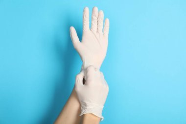 Doktor açık mavi arka plana tıbbi eldiven takıyor, yakın plan.