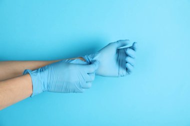 Doktor açık mavi arka plana tıbbi eldiven takıyor, yakın plan.