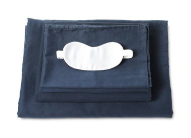 Beyaz arka planda ipeksi çarşaf ve uyku maskesi yığını.