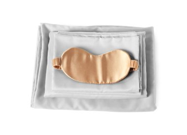 Beyaz arka planda ipek çarşaflar ve uyku maskesi.