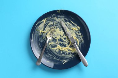 Açık mavi arka planda kirli tabak ve çatal bıçak takımı.