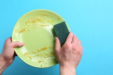 Açık mavi arka planda süngerle kirli tabakları yıkayan adam, yakın plan. Metin için boşluk