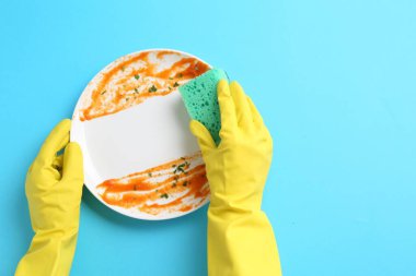 Açık mavi arka planda süngerle kirli tabakları yıkayan adam, üst manzara. Metin için boşluk