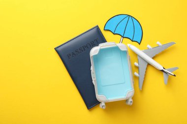 Seyahat sigortası. Uçak modeli, pasaport, kağıt şemsiye ve sarı arka planda bavul. Metin için boşluk