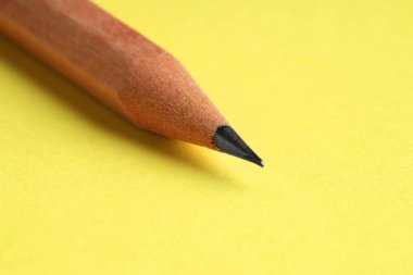 Sarı arka planda keskin bir grafit kalem, yakın plan.