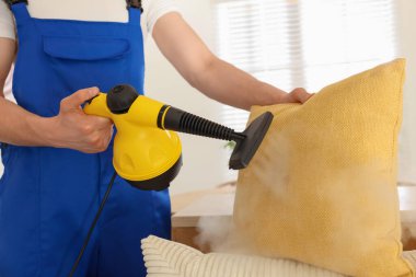 Temizlikçi yastığı evde buhar temizleyicisiyle temizliyor.