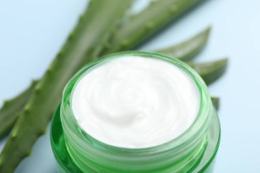 Aloe vera özütüyle nemlendirici krem ve açık mavi arkaplanda yapraklar, yakın plan.