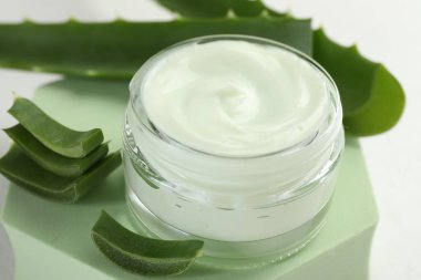 Aloe vera özütüyle nemlendirici krem, beyaz arka planda kesim yaprakları ve podyum, yakın plan