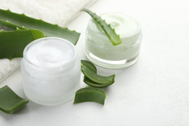 Aloe vera özütüyle nemlendirici krem, beyaz desenli arka planda yapraklar ve havlu, yakın plan