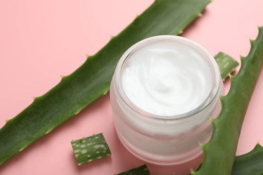 Kavanozda aloe vera özütüyle nemlendirici krem ve pembe arka planda yapraklar, yakın plan