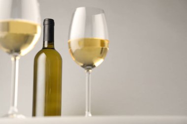 Gözlüklü lezzetli beyaz şarap ve açık gri arka planda şişe, düşük açılı manzara. Metin için boşluk