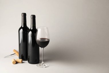 Bardakta kırmızı şarap, şişeler, mantarlar ve açık gri arka planda tirbuşon, metin için yer