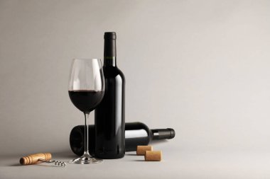 Bardakta kırmızı şarap, şişeler, mantarlar ve açık gri arka planda tirbuşon, metin için yer