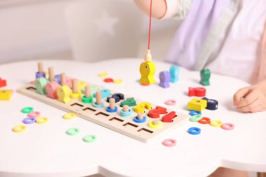 Motor beceri geliştirme. Küçük kız matematik oyunuyla oynuyor. Beyaz masada sayıları avlıyor. Kapalı mekanda.