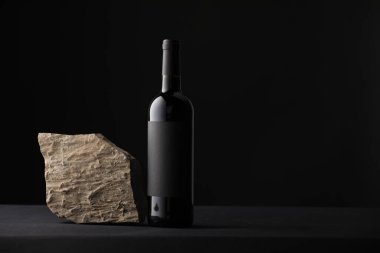 Siyah masada bir şişe şarap ve taş, metin için yer.