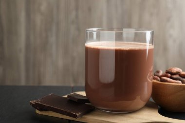 Lezzetli çikolatalı süt, barlar ve kakao çekirdekleri siyah ahşap masada, yakın plan. Metin için boşluk