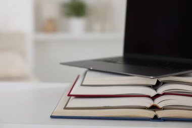 Beyaz masadaki farklı kitap ve dizüstü bilgisayar kapalı, yakın plan.