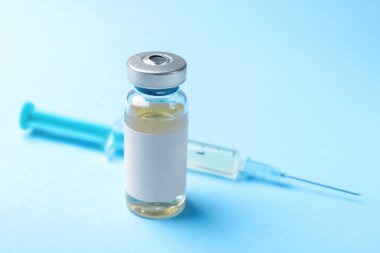 Cam şişede Hepatit aşısı ve açık mavi arka planda şırınga, yakın plan