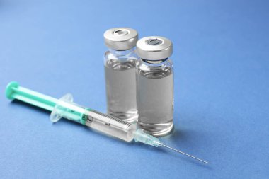 Cam şişelerde Hepatit aşısı ve mavi arka planda şırınga.