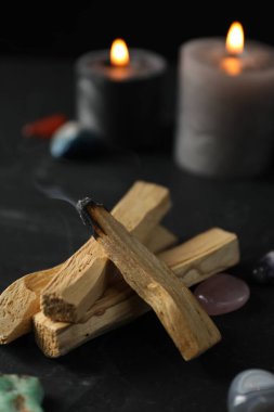 Yanan palo santo sopası, değerli taşlar ve yanan mumlar siyah masada, yakın plan.