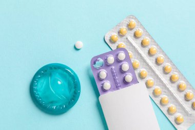 Açık mavi arka planda doğum kontrol hapı ve prezervatif kabarcıkları var.