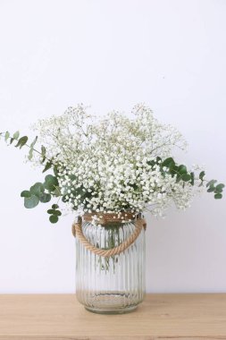 Güzel çikila çiçekleri ve okaliptüs dalları beyaz duvarın yanındaki ahşap masada.