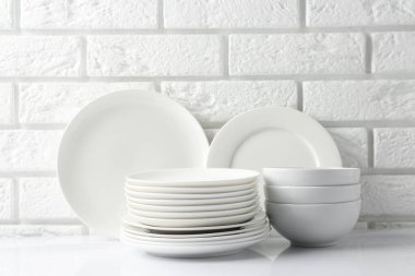 Different clean dishware on white table near brick wall