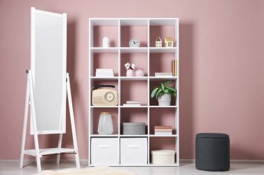 İçerideki pembe duvarın yanında dekor ve ayna olan raf ünitesi.