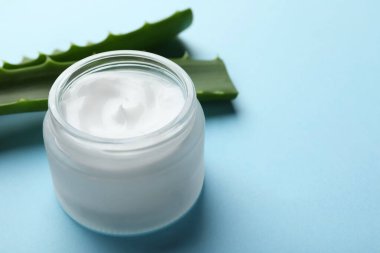 Açık mavi arka planda krema ve aloe yaprakları, yakın plan. Metin için boşluk