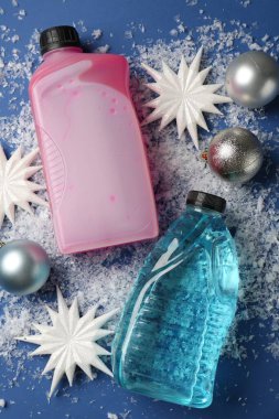 Plastik şişelerde antifriz, takılar, dekoratif kar taneleri ve mavi arka planda buz, düz bir zemin.