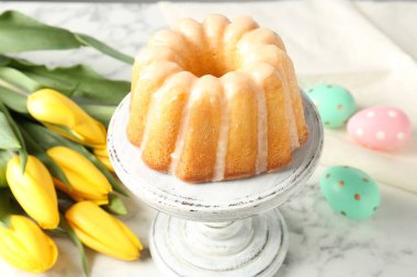 Lezzetli kek, Paskalya yumurtası ve laleler beyaz mermer masada, yakın plan.