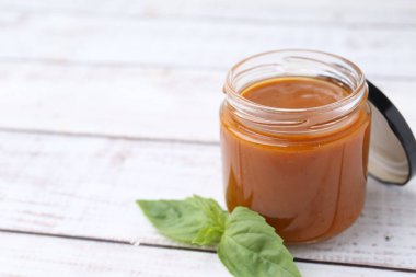 Cam kavanozda lezzetli köri sosu ve beyaz ahşap masada fesleğen, yakın plan. Metin için boşluk