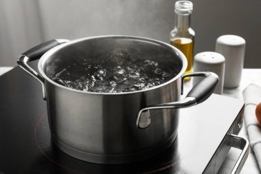 Kaynar suyla tencereyi pişirmek ve arka plandaki gri ışığa karşı soba, yakın plan