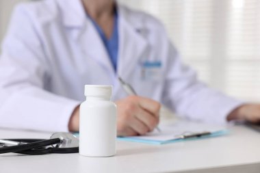 Hastanedeki beyaz masada çalışan profesyonel doktor steteskop ve bir şişe hapa odaklanıyor.