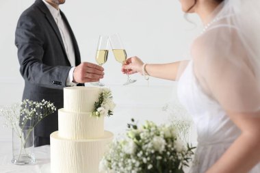 Evde düğün pastası olan evli bir çift şampanya bardaklarını tokuşturuyor.