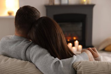 Çift kanepede, şık şömineli, arka manzaralı bir odada birlikte vakit geçiriyor.