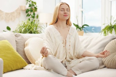 Feng shui. Evdeki kanepede meditasyon yapan genç bir kadın.