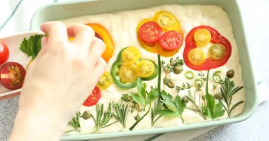 Açık gri masadaki çiğ Focaccia 'ya maydanoz ekleyen kadın.